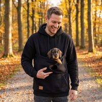 Mann im schwarzen Hoodie mit Kuscheltasche, Dackelwelpe schaut heraus