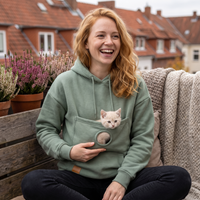 Frau im grünen Hoodie mit Kuscheltasche, ein Kätzchen schaut heraus